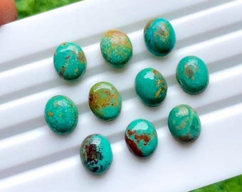 May include: A collection of ten oval-shaped turquoise gemstones with brown and gold matrix patterns. The stones are arranged on a white surface, showcasing their polished, smooth surfaces and vibrant teal color.
