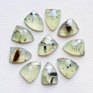 May include: Ten faceted, triangular-shaped gemstones in a pale, translucent green hue. Each stone features unique, dark, needle-like inclusions scattered throughout the interior, creating a distinct pattern within the polished, geometric surfaces.