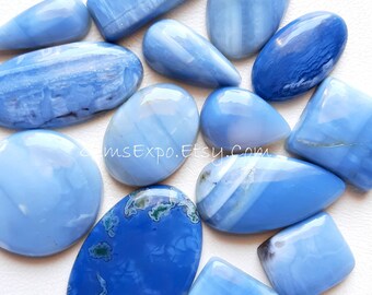 May include: A collection of polished blue opal gemstones in various shapes, including oval, teardrop, and rectangular. The opals display a range of light to deep blue hues with subtle patterns and swirls. Some stones have white or green inclusions.