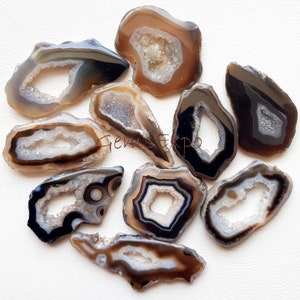 Puede incluir: Una colección de geodas de ágata pulidas de diversas formas y tamaños. Las geodas presentan bandas de color marrón, negro y blanco, con centros cristalinos. La estética general es natural y terrosa, adecuada para la creación de joyas o exhibición.