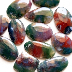Puede incluir: Una colección de 11 piedras de ágata pulidas de forma ovalada, de color verde, rojo y morado. Las piedras presentan una variedad de patrones y colores.