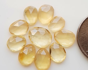Pode incluir: Uma coleção de nove pedras preciosas de citrino amarelo facetadas, cada uma com uma forma e um tamanho únicos. As pedras estão dispostas em círculo sobre um fundo branco, com um centavo de euro para a escala.
