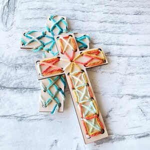 May include: Two wooden crosses with colorful yarn embroidery. One cross is blue and green, the other is orange and white.