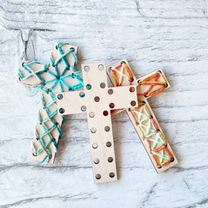 May include: Three wooden cross shapes with different colored string woven through the holes. The crosses are arranged in a triangular shape.