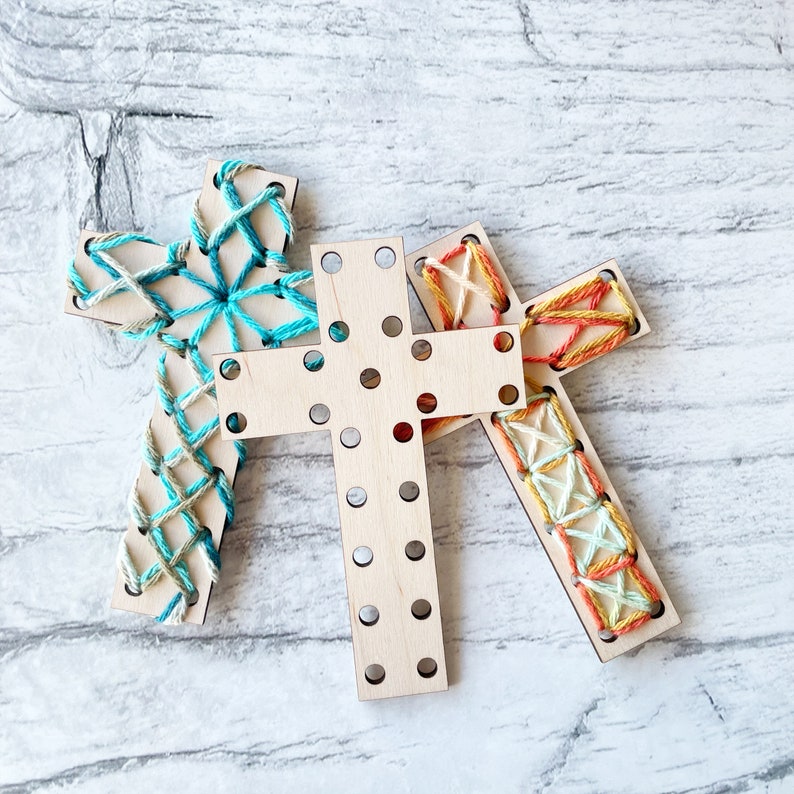 May include: Three wooden cross shapes with different colored string woven through the holes. The crosses are arranged in a triangular shape.