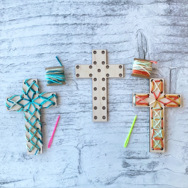 May include: Three wooden cross shapes with holes for stringing yarn. One cross is blue and green, one is orange and yellow, and one is plain wood. Each cross comes with a spool of yarn and a needle.