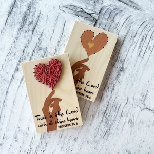 Może przedstawiać: Dwa drewniane znaki z tekstem "Trust in the Lord with all thine heart Proverbs 35-6" i "the Lord thine heart Proverbs 35-6". Każdy znak zawiera czerwone serce wykonane ze sznurka.