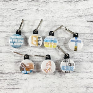 May include: Six zipper pulls with round buttons featuring inspirational Christian quotes. The buttons are white with blue, yellow, and black text. The quotes include "You called me out upon the waters", "Until God opens the next door", "Child of God", "Give your heart", "Tell your mountain about your God", and "What would Jesus do?"