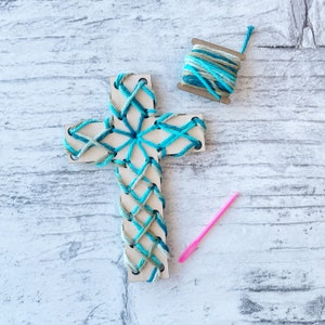 May include: A wooden cross with blue and green yarn woven into a pattern. A spool of yarn and a pink needle are also included.