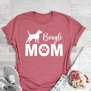 Op de afbeelding: Koraalroze T-shirt met een wit silhouet van een beagle en de tekst "Beagle Mom" met een pootprint.