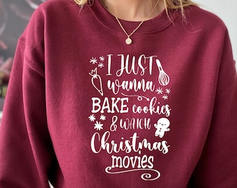 May include: A maroon sweatshirt with the text "I just wanna bake cookies & watch Christmas movies" in white. The text is surrounded by stars and includes a carrot, a whisk, and a gingerbread man.