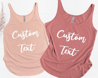 May include: Two tank tops with the text "Custom Text" in white lettering. The tank top on the left is a light pink color and the tank top on the right is a darker pink color. The tank top on the left is labeled "Desert Pink" and the tank top on the right is labeled "Paprika".