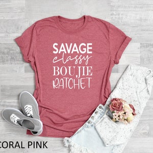 May include: Coral pink t-shirt with the text "SAVAGE classy BOUJIE RATCHET" in white lettering.