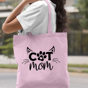 Pode incluir: Sacola de tecido rosa claro com um design de pata de gato preto e o texto "CAT MOM".