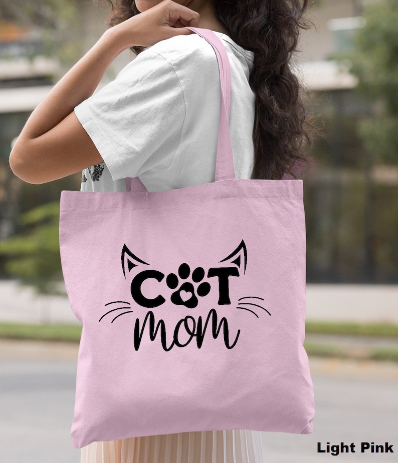 Pode incluir: Sacola de tecido rosa claro com um design de pata de gato preto e o texto "CAT MOM".
