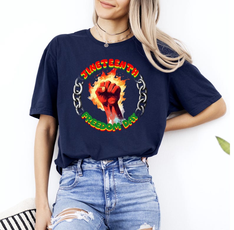 May include: Navy blue t-shirt featuring a circular graphic with the text "Juneteenth Freedom Day." The design includes a raised fist in red, surrounded by flames and a chain border. The text is in green and yellow.