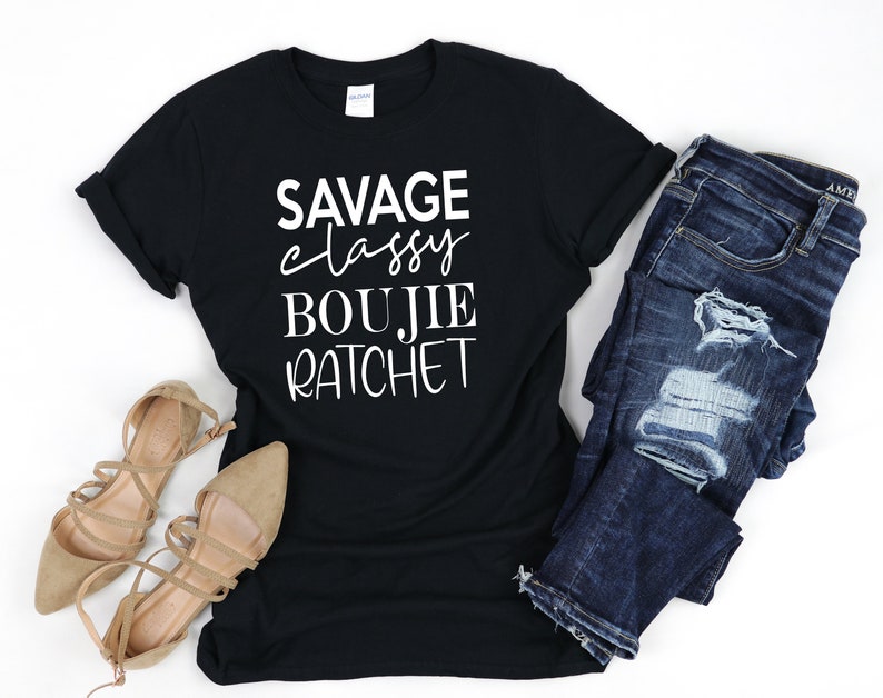 May include: Black t-shirt with white text that reads "Savage Classy Boujie Ratchet". The shirt is paired with blue jeans and brown sandals.