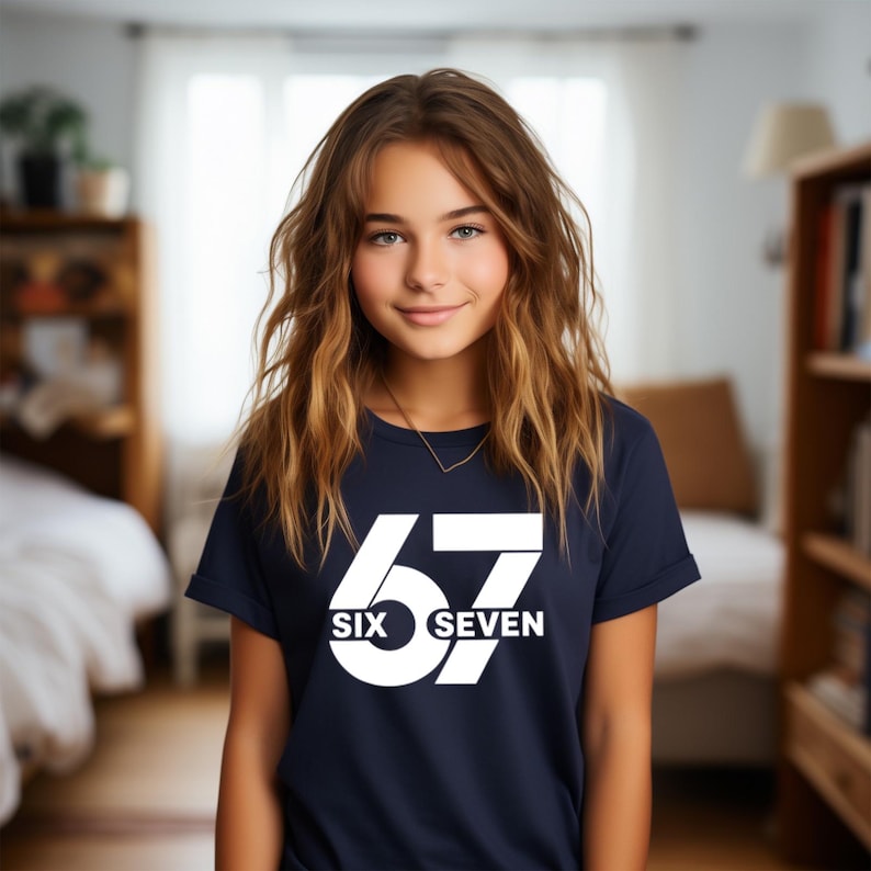 May include: Navy blue t-shirt with the number "67" in white, with "SIX SEVEN" below. The t-shirt is worn by a person with long, wavy brown hair.