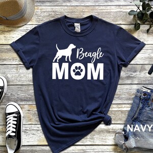 Op de afbeelding: Donkerblauw T-shirt met een wit silhouet van een beagle-hond en de tekst "Beagle MOM" met een pootprint.