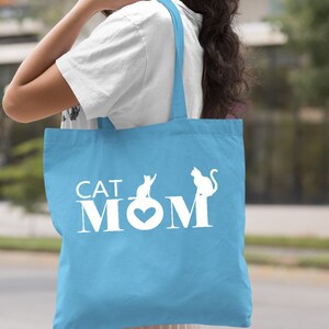 Puede incluir: Bolsa de tela azul claro con texto blanco que dice "CAT MOM" con dos siluetas de gatos.