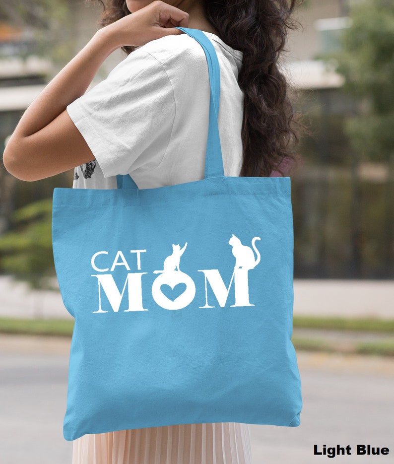 Puede incluir: Bolsa de tela azul claro con texto blanco que dice "CAT MOM" con dos siluetas de gatos.