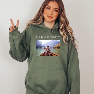 May include: A green hooded sweatshirt with a pocket on the front. The sweatshirt has a photo of a couple in a boat on a lake with mountains in the background. The text "YOUR PHOTO HERE" is printed above the photo.