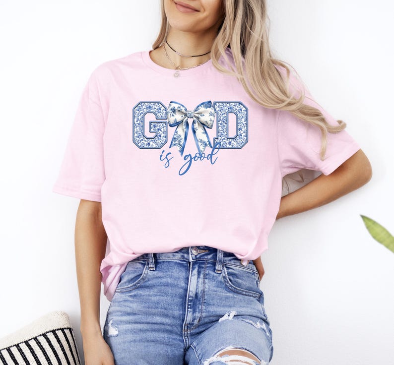 K&ouml;nnte beinhalten: Ein pinkfarbenes T-Shirt mit einem blauen und wei&szlig;en Schleifen-Motiv und dem Text "GOD is good".