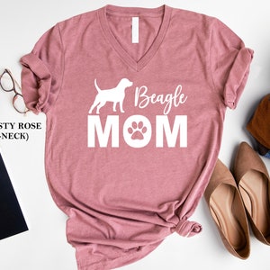 Op de afbeelding: Stofkleurig roze V-hals T-shirt met een wit silhouet van een beagle en de tekst "Beagle Mom" met een poot afdruk.