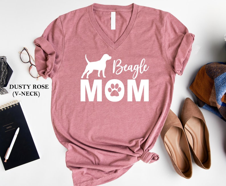 Op de afbeelding: Stofkleurig roze V-hals T-shirt met een wit silhouet van een beagle en de tekst "Beagle Mom" met een poot afdruk.