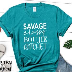 May include: A teal blue t-shirt with the text "Savage Classy Boujie Ratchet" printed in white.