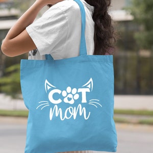 Pode incluir: Sacola de tecido azul claro com texto branco que diz "CAT mom" com uma pegada de pata e orelhas de gato.