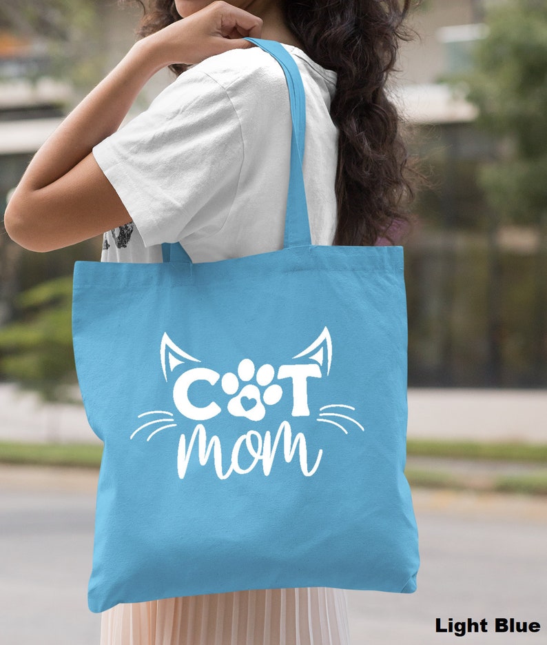 Pode incluir: Sacola de tecido azul claro com texto branco que diz "CAT mom" com uma pegada de pata e orelhas de gato.
