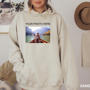 May include: A beige hoodie with a large pocket on the front. The hoodie has the text "YOUR PHOTO HERE" printed on the front, and a photo of a couple in a boat on a lake is below the text.