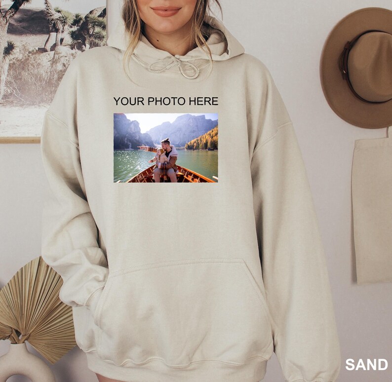 May include: A beige hoodie with a large pocket on the front. The hoodie has the text "YOUR PHOTO HERE" printed on the front, and a photo of a couple in a boat on a lake is below the text.