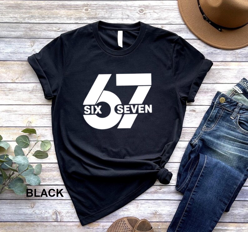 May include: Black t-shirt with a large white graphic of the number 67. The word "SIX" is centered below the 6 and the word "SEVEN" is centered below the 7. The word "BLACK" is printed at the bottom left of the shirt.