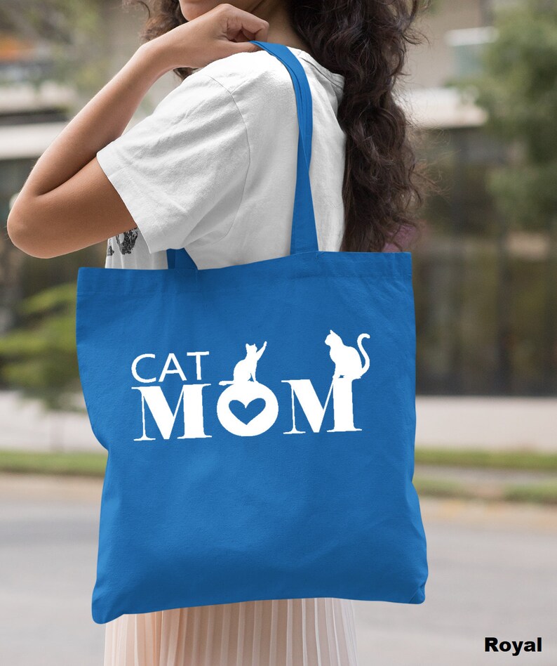Puede incluir: Una bolsa de tela azul real con asas blancas y el texto "CAT MOM" en blanco con un coraz&oacute;n blanco y dos siluetas de gatos blancas.