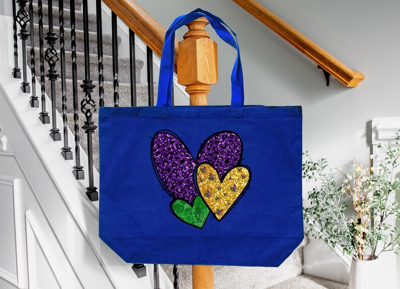 Puede incluir: Una bolsa de lona azul con un dise&ntilde;o de coraz&oacute;n de purpurina morado, dorado y verde. Los corazones est&aacute;n superpuestos.