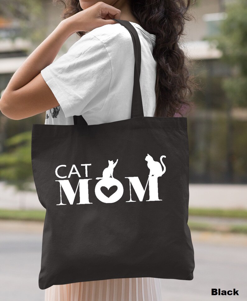 Puede incluir: Bolsa de tela negra con texto blanco que dice "CAT MOM" con un coraz&oacute;n y dos siluetas de gatos.