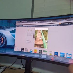 May include: A computer monitor displaying a webpage with a delivery photo. The photo shows a small package on a brick pathway next to a green painted border. The monitor is on a wooden desk.