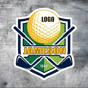 Puede incluir: Un logotipo de golf verde y azul con un contorno blanco. El logotipo presenta una bola de golf con la palabra "LOGO" en ella, dos palos de golf cruzados y el texto "JAMESON" y "YEAR".
