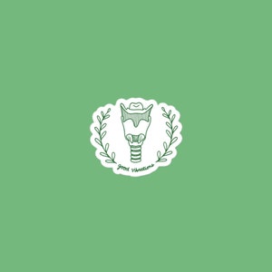 Op de afbeelding: Een witte sticker met een groene omtrek toont een lijntekening van de menselijke larynx met een krans van bladeren eromheen. De tekst "Good Vibrations" staat onder de larynx.