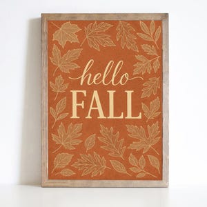 Op de afbeelding: Een rechthoekig wandbord met een lichtbruine houten lijst en een roestoranje achtergrond. De tekst hello FALL staat in het midden in een crèmekleur, omringd door een patroon van crèmekleurige lijntekeningen van herfstbladeren.