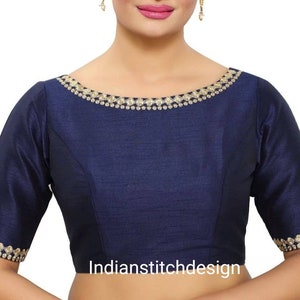May include: A navy blue sleeveless blouse with a gold embroidered neckline and trim around the sleeves. The blouse has a scoop neckline and is made of a soft, silky fabric.