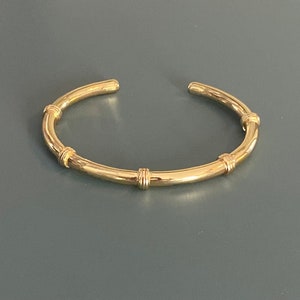 May include: A gold bangle bracelet with a smooth, rounded design and four decorative accents.