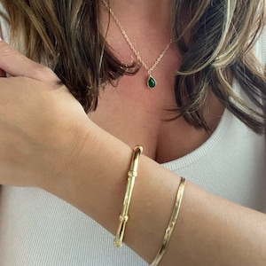 May include: Two gold bracelets on a person's wrist. The bracelet on the bottom is a thin, flat band. The bracelet on top is a thicker, round band with a textured design.