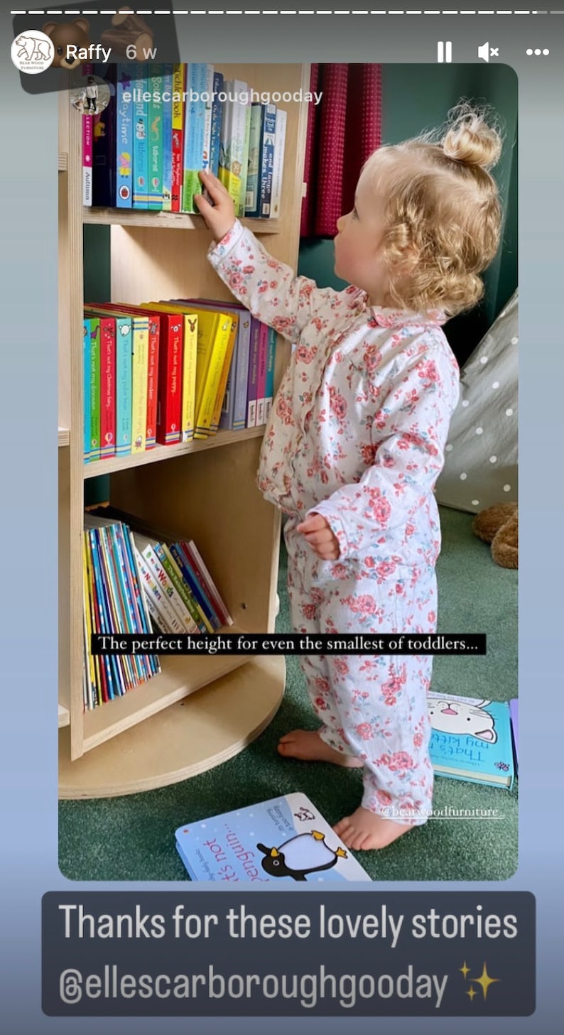 May include: A white wooden bookshelf with three shelves, filled with colorful children's books. A young child in a floral print pajamas reaches for a book on the top shelf. The text "The perfect height for even the smallest of toddlers..." is visible below the bookshelf. The text "Thanks for these lovely stories @ellescarboroughgooday" is visible at the bottom of the image.