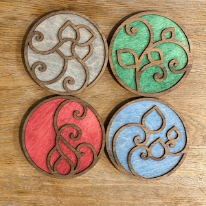 May include: Four round wooden coasters with a decorative design of a vine with leaves. The coasters are painted in different colors: gray, green, red, and blue.