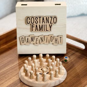 May include: A wooden game night box with the words "Costanzo Family Game Night" engraved on the front. The box contains a wooden game with wooden pegs and a blue and green dice.
