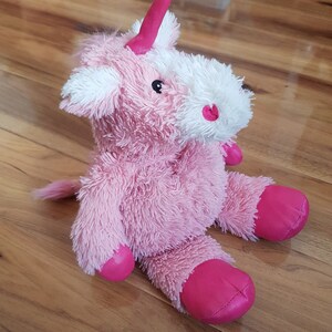 Könnte beinhalten: Rosa Plüsch-Einhorn-Spielzeug mit weißem Gesicht und rosa Hufen. Das Einhorn hat ein rosa Horn und schwarze Augen.