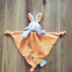 May include: An orange and white plush bunny comfort blanket. The bunny has long ears and a sweet face. The blanket has the word "love" embroidered on it in gold thread with blue accents. A small tag is attached.
